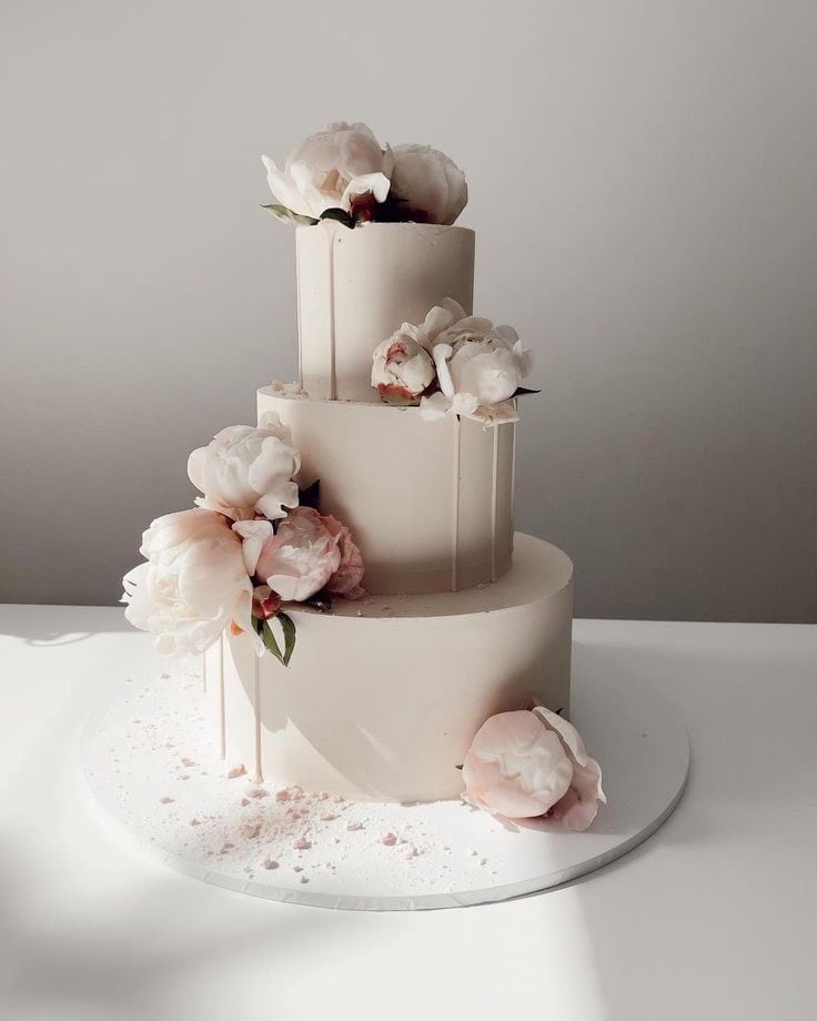 Elegant three-tier white wedding cake with soft pink peonies and delicate decoration, perfect for special celebrations.