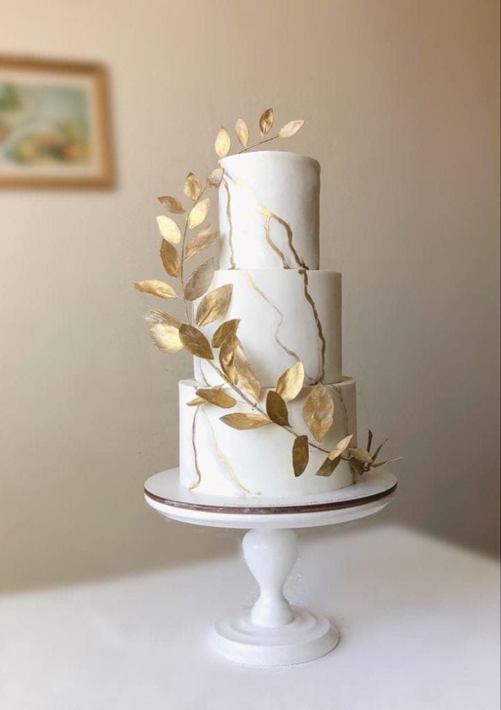 Elegant multi-tiered wedding cake with gold leaf accents and decorative leaves for celebration events.