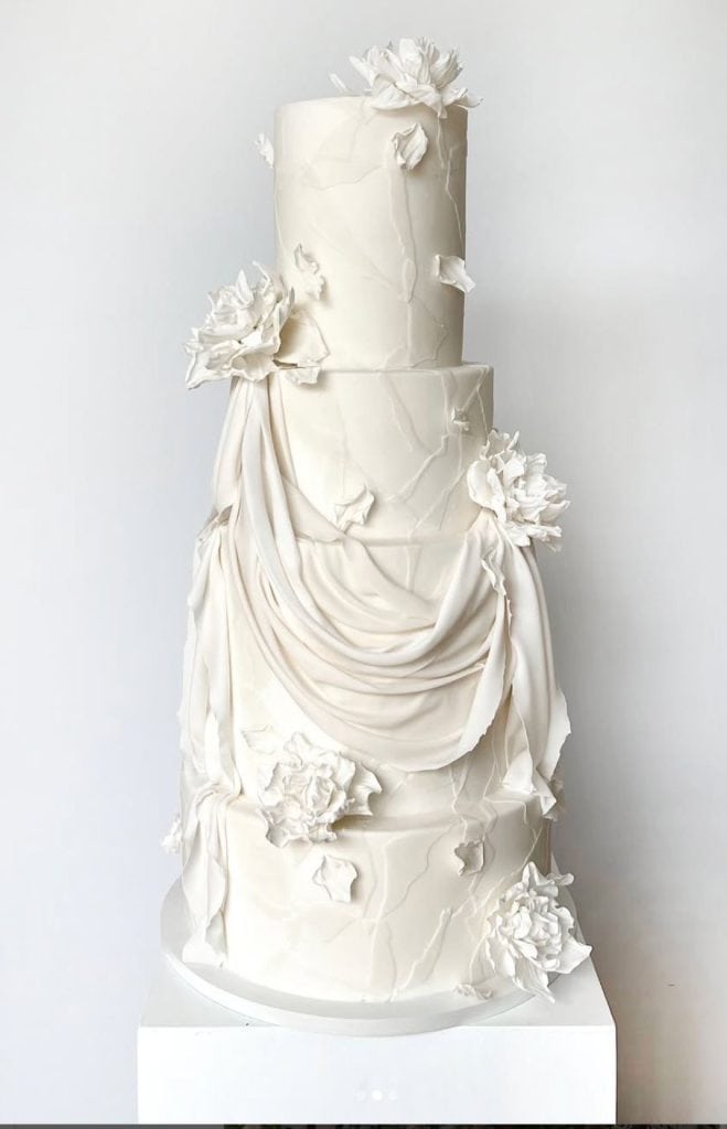 Elegant white wedding cake with floral fondant decorations and draped icing. Perfect for wedding celebrations.